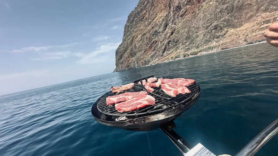 Steaks on the grill on deck, with sea cliffs behind